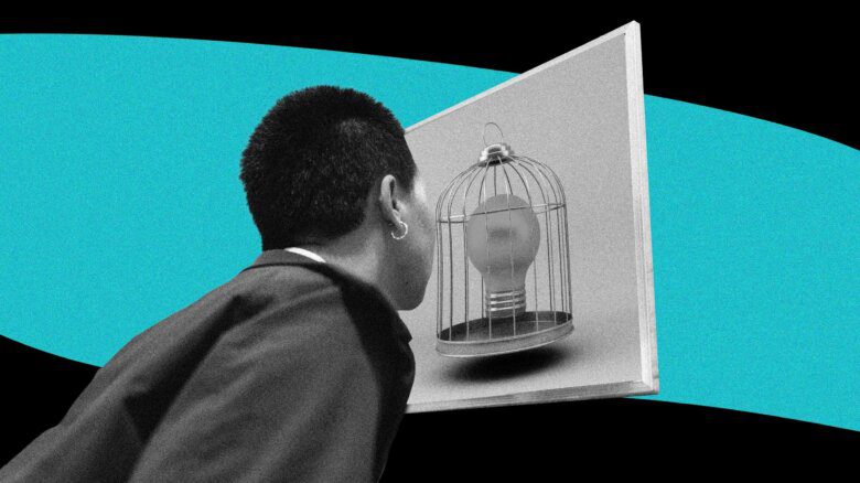 A person with short dark hair is seen from behind; they are facing a birdcage with a lightbulb inside of it.