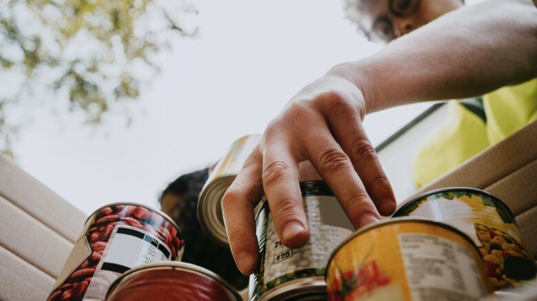 Photo of a person reaching into a box to grab a can of food from a stack